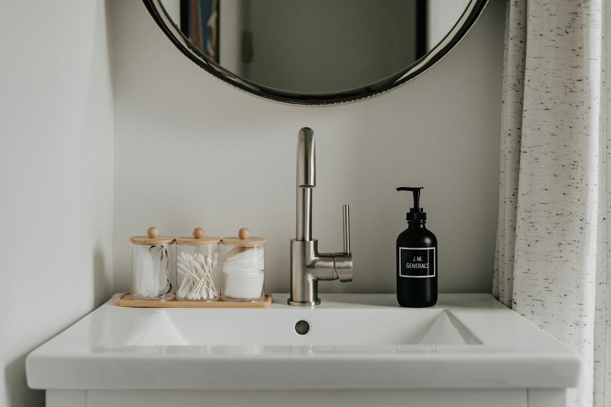 A clean washroom sink with a soap dispenser and a round mirror