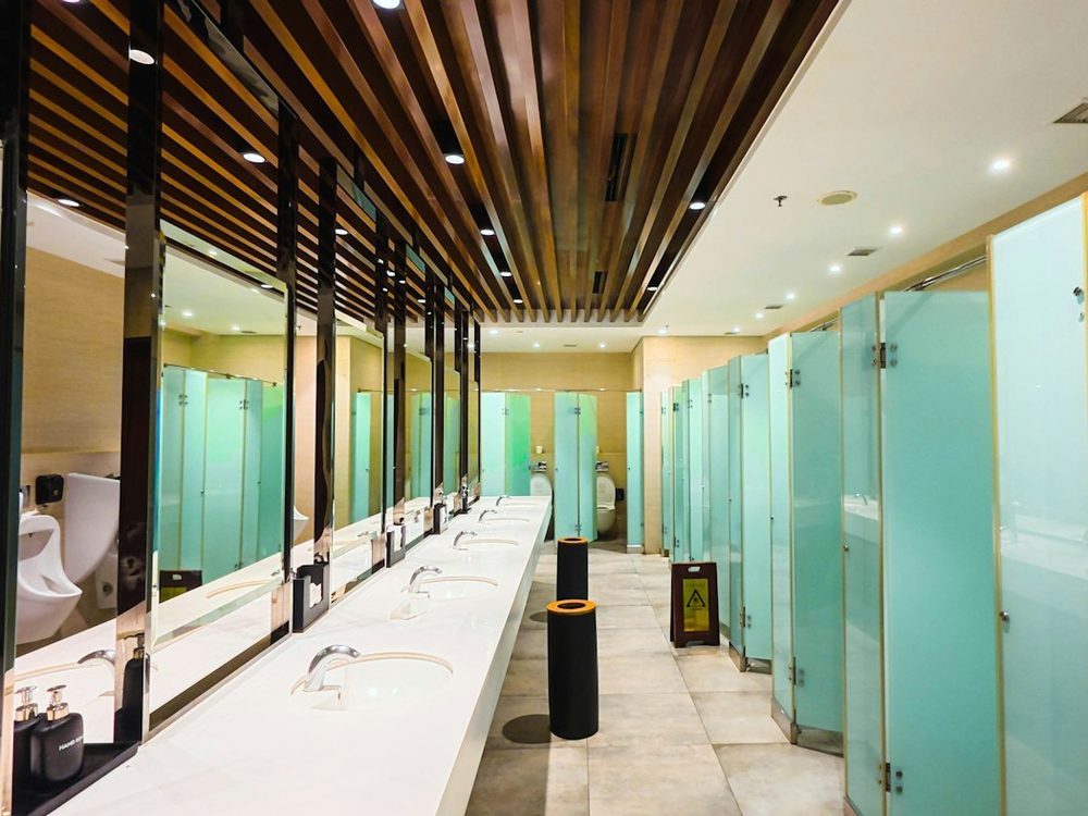 A bright, spotless washroom with a long row of basins, frosted cubicles and a wet floor sign
