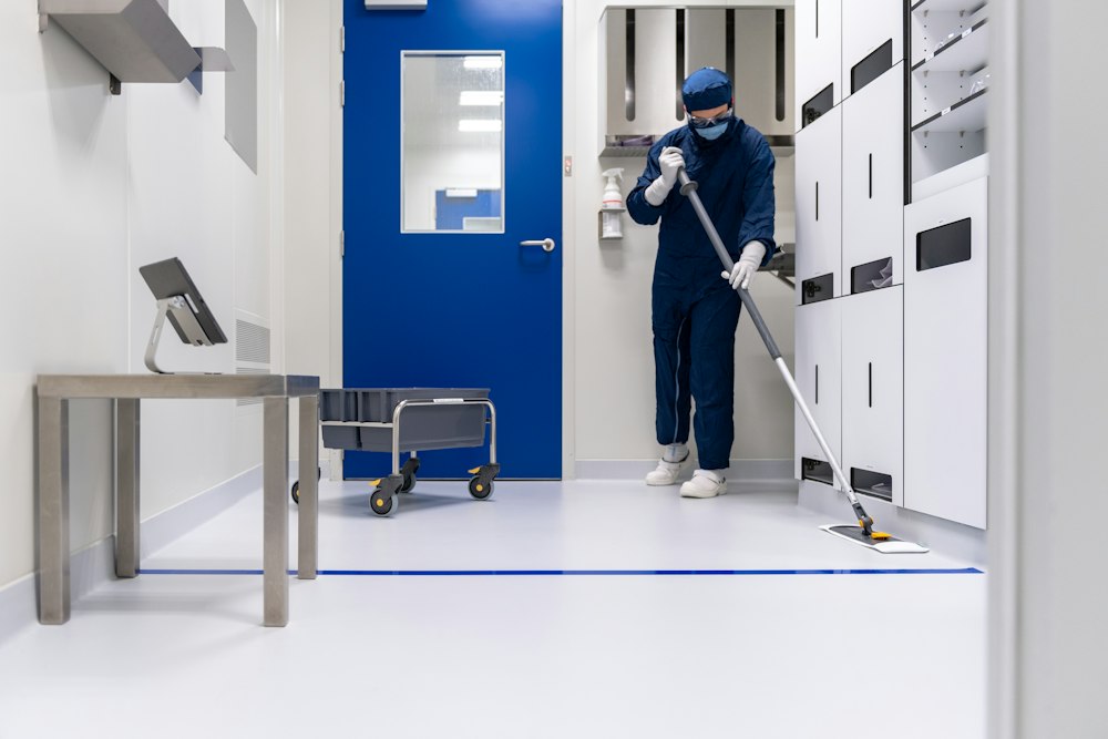 A cleaner in scrubs mopping a clean, clinical room