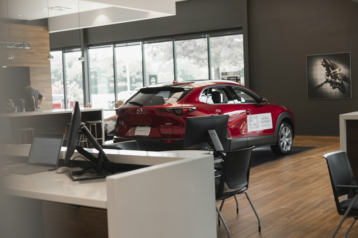 A modern car showroom with a red car, glass frontage and sales desk