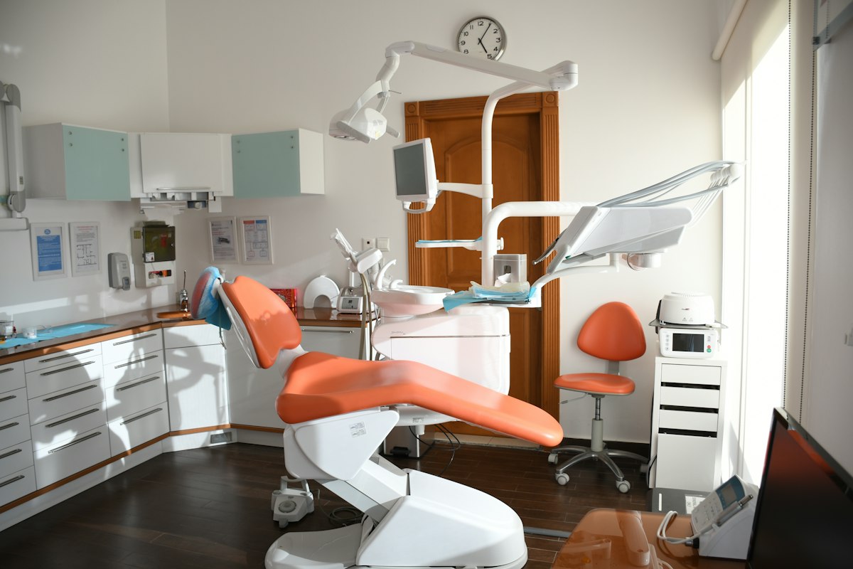 A bright dental treatment room with an orange chair and clinical equipment