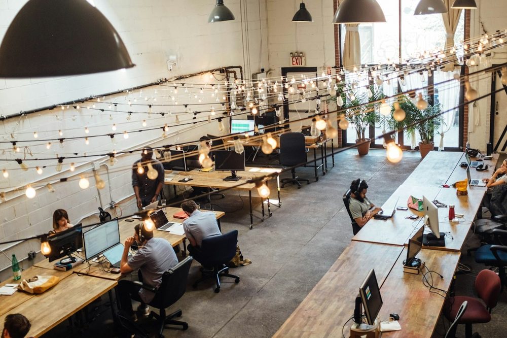 A long shared workspace with string lights and people working at wooden desks, the kind of Farringdon office we clean