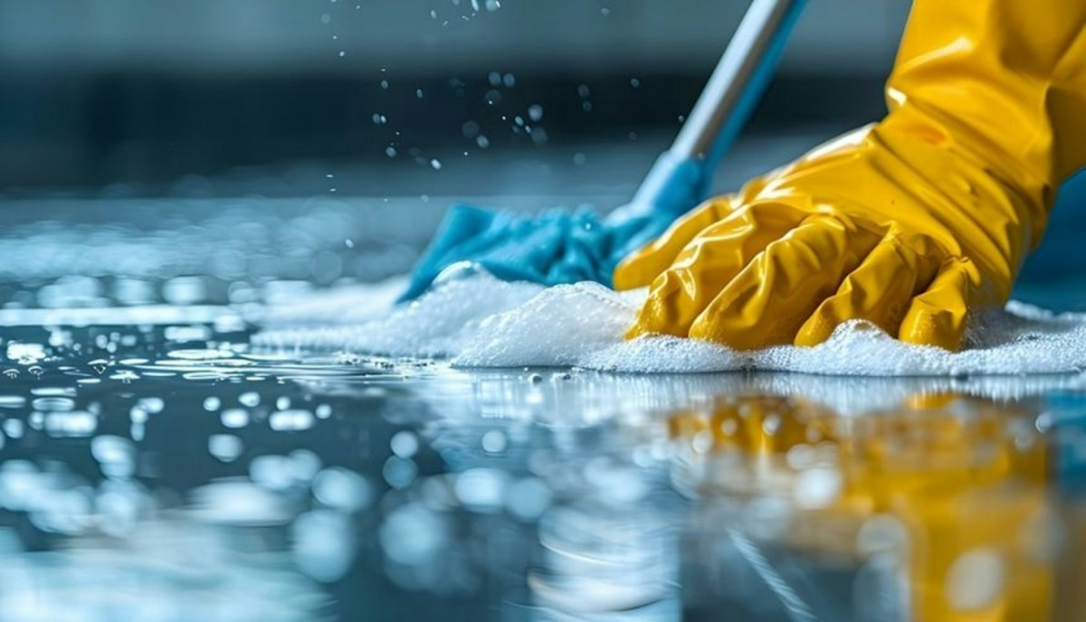 A gloved hand scrubbing a floor with a cloth and cleaning foam, the kind of detail work a post-build clean involves