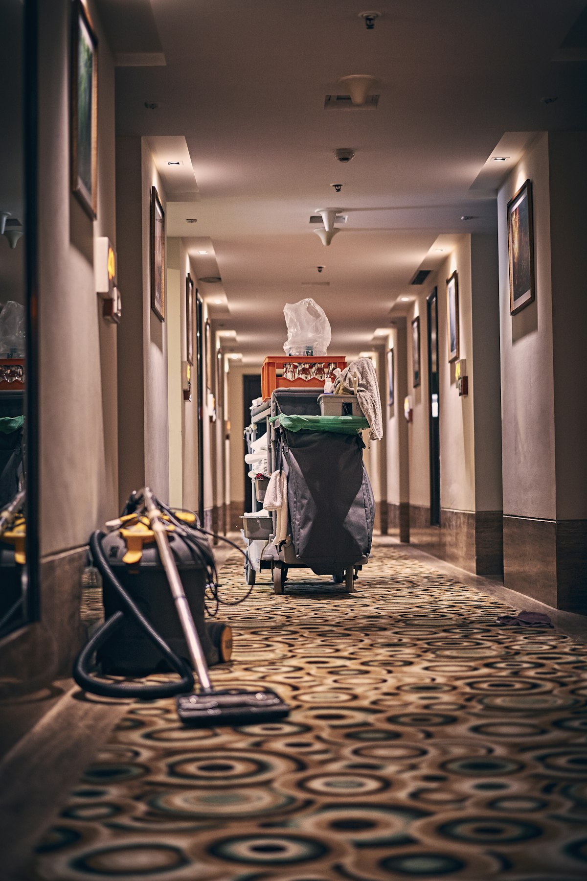 A cleaner's trolley and vacuum in a long carpeted corridor
