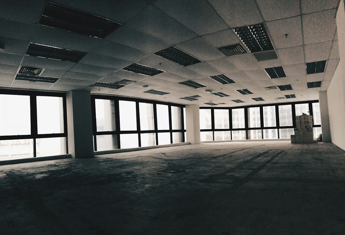 A large empty office floor with big windows and a dusty concrete floor