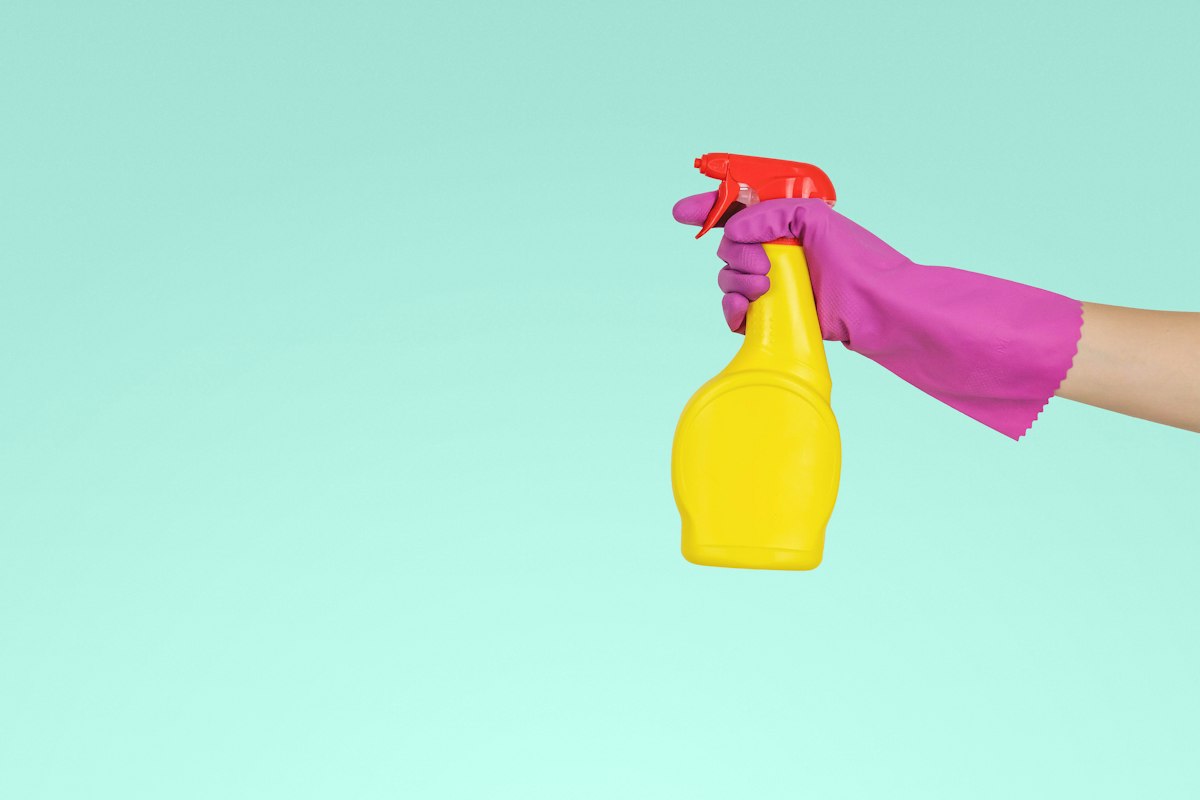 A gloved hand holding a cleaning spray bottle, ready for a top-to-bottom deep clean