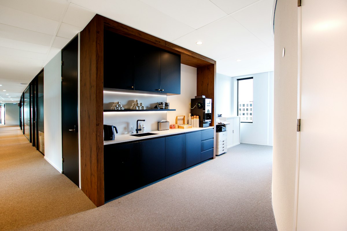 A modern office kitchen with dark cabinets and a white worktop